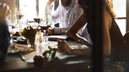 Blurry close-up of people eating at restaurant table with white wine glass in middle
