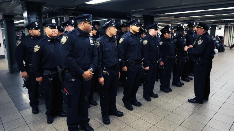 Rows of uniformed NYPD transit officers stand at attention in NYC subway station.