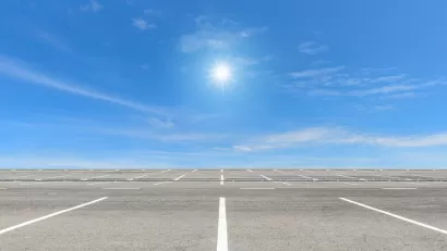 Vast, empty parking lot with blue sky and bright sun in background