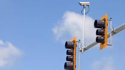 Stoplight with two lights and mounted traffic camera against blue sky with white clouds