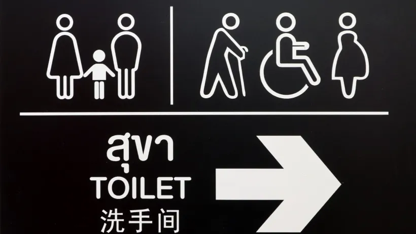 White on black restroom sign with symbols and text in Thai.