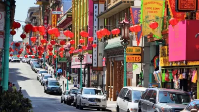 View of street in Chinatown, San Francisco with cars parked along curb and red Chinese lanterns hanging above street
