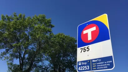 Close-up of red and blue MetroTransit bus stop sign against blue sky and green tree in New Hope, Minnesota