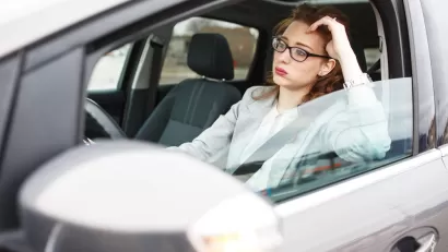 Woman in car stuck in traffic, leaning on her elbow in frustration