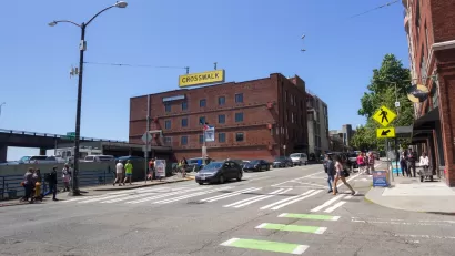 Pedestrians in zebra crosswalk with green bike lane in downtown Seattle, Washington with three-story brick building in background