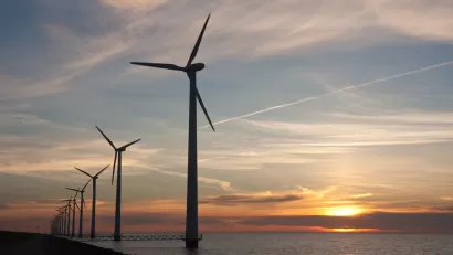 Line of offshore wind turbines with sunset over sea in the background