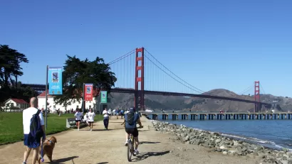 People walking and biking on flat dirt trail next to San Francisco Bay with Golden Gate Bridge in background