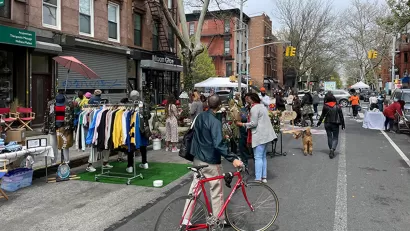 Man with red bicycle walks bike down 'open street' with vendor booths in New York City.