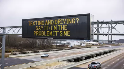 Digital highway sign above six-lane highway that says, "Texting and Driving? Say It: I'm the Problem It's Me."