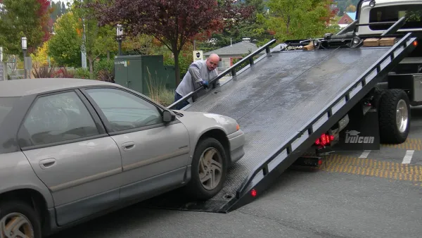 A grey car being loaded onto a flatbed truck