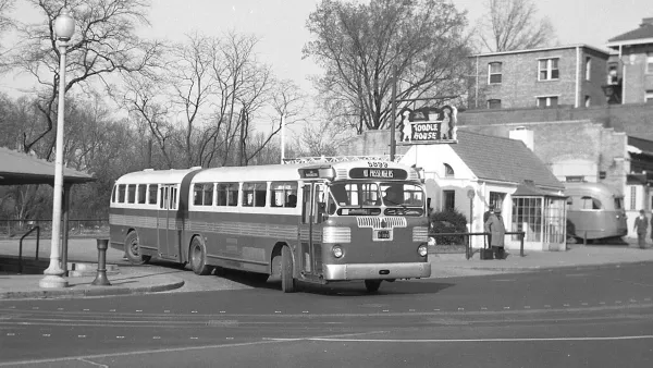 Black and white photo of articulated bus turning out of parking lot in the 1940s.