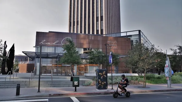 Person on small black e-bike riding on street in front of Wells Fargo Center building in Los Angeles.