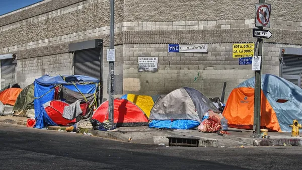 Tents inhabited by unhoused people lined up on sidewalk in Los Angeles, California in front of industrial building.