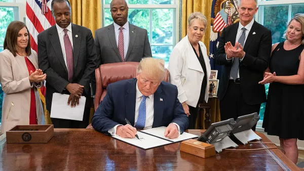Donald Trump signing executive order in Oval Office with other officials behind him.