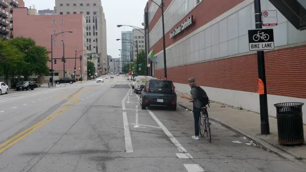 Man on bike looking back at camera with black car blocking bike lane in front of him.