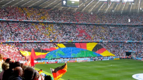 Soccer stadium in Berlin during 2006 World Cup full of fans waving German flags and a banner showing earth and radiant rays formed by bottom section of crowd.