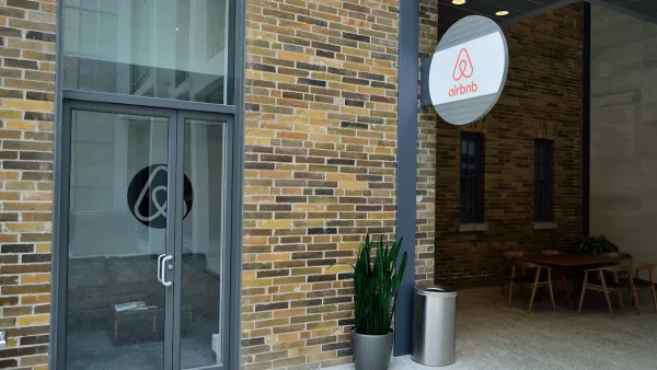 A brick building with a circular sign with the Airbnb logo hanging off of it.