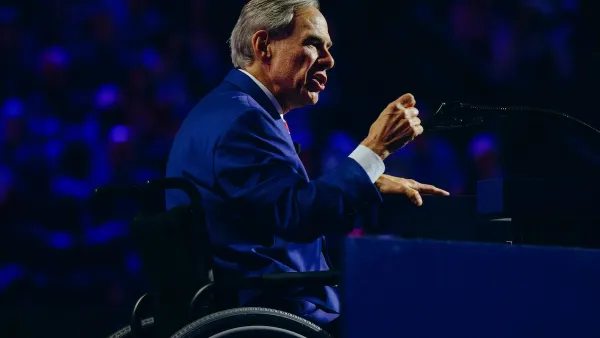 Gov. Abbot gestures with his hand at a convention. He is wearing blue and is in his wheelchair.