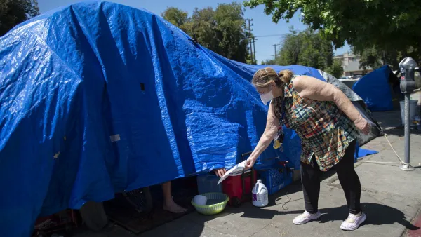 Outreach worker wearing mask reaches into blue tarp with unhoused person to hand them a pamphlet.