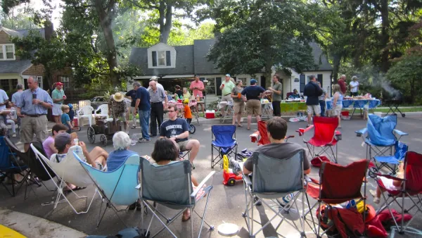 People sitting in lawn chairs on residential street having block party.