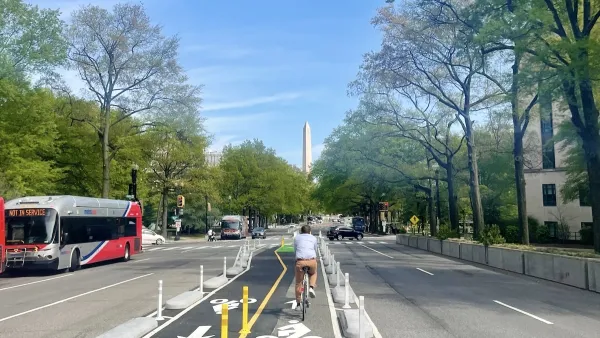 Cyclist on protected bike lane in middle of street in Washington D.C. with Washington Monument obelisk visible in background.