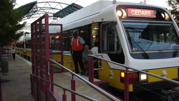 White DART light rail train at platform in Plano, Texas with conductor standing outside of door.