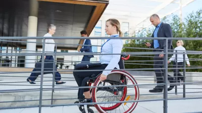 Woman in wheelchair using outdoor accessibility ramp with people walking in background