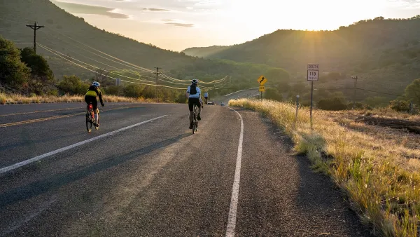 Cyclists on an empty rural paved road with hills and sunset in background.