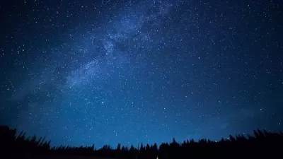 View of dark night sky with visible Milky Way over dark forest.