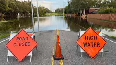 Orange and black "Road Closed" and "High Water" signs blocking a flooded roadway in Florida after a hurricane.