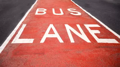 Close-up of red and white BUS LANE sign painted in street lane.