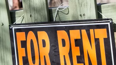Close-up of orange and black For Rent sign on green wood fence.