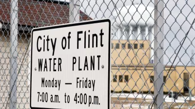 Close-up of sign on chain link fence "City of Flint Water Plant" with hours.