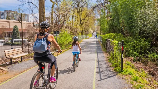 Family wearing helmets rides down separated bike trail in city.