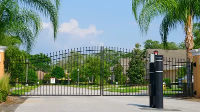 Closed black wrought iron gate in front of gated residential community with large palm trees along sides of street.