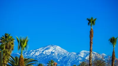 Tall palm trees against bright blue sky with snowy mountains in background. Los Angeles, California.