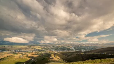 Distant view of Lewiston, Idaho nestled in green hills against cloudy blue sky