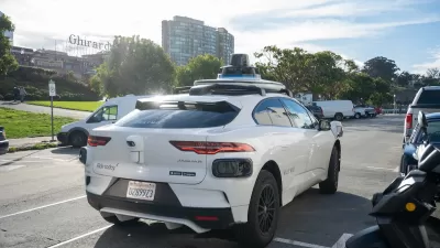 White Waymo autonomous vehicle in parking area in San Francisco, California with Ghirardelli vintage sign in background.