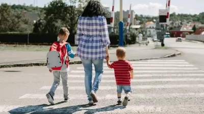 Woman walking two small children across crosswalk.