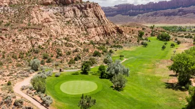 Aerial view of green colf course next to rocky desert cliffs in Moab, Utah