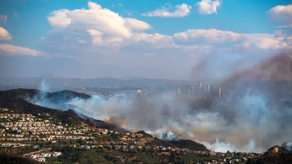 Heavy smoke from Palisades Fire burning in hillsides with homes with downtown Los Angeles visible in background.