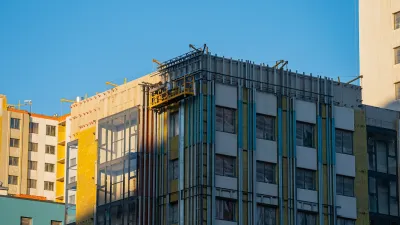 Construction workers on a suspended platform are installing thermal insulation on the facade of a modern apartment building, improving energy efficiency and reducing heat loss during cold weather.