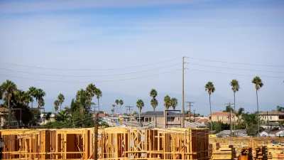 Wood-frame apartment building under construction with tall palm trees and power lines in background.