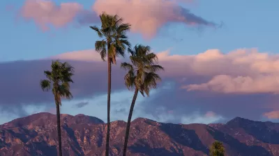 Twilight view of San Gabriel Mountains with three tall palm trees in foreground and purpleish sky.