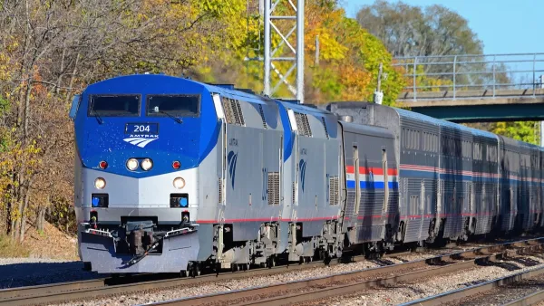 Blue and silver Amtrak train with vibrant green and yellow foliage in background.
