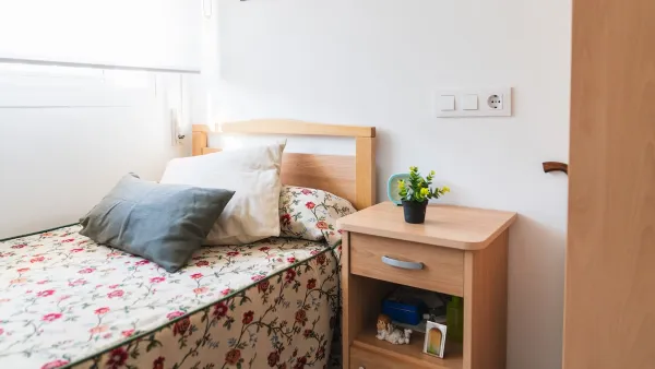 Small, brightly lit bedroom with flowery sheets on single bed in supportive housing or nursing home.
