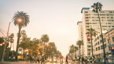 Busy pedestrian crosswalk on wide boulevard in Santa Monica, California lined with tall palm trees against golden hour light.