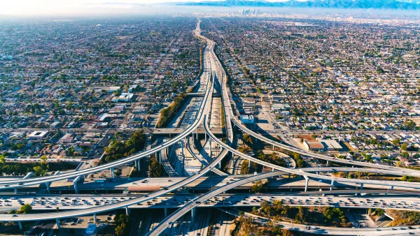 Aerial view of freeway interchange in Los Angeles with low-rise housing on either side and mountains in the background