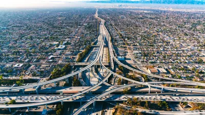 Aerial view of freeway interchange in Los Angeles with low-rise housing on either side and mountains in the background