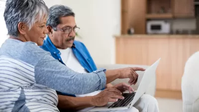 Senior couple sitting on sofa looking at laptop computer held in the man's lap.